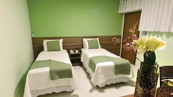 A hotel room with two single beds, a nightstand, a vase with flowers, and a wooden door.