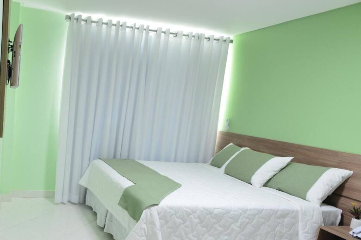 Quarto de hotel com cama, cortinas e parede verde.