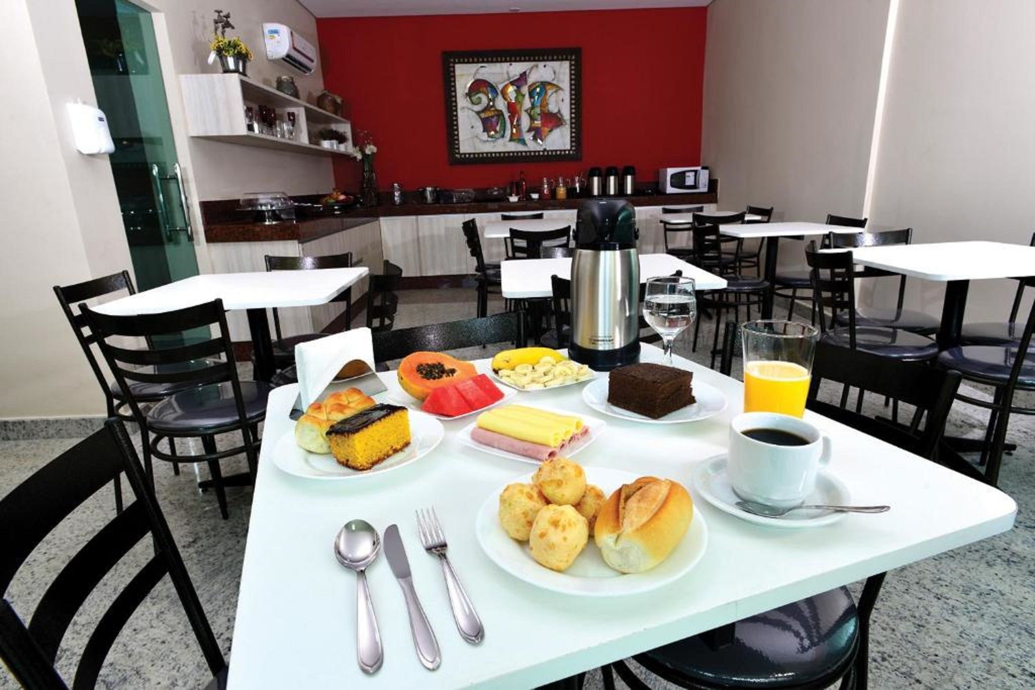 Uma área de refeições com mesas, cadeiras e diversos alimentos, incluindo doces, frutas e bebidas.