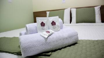 Una cama bien hecha con ropa de cama blanca y verde, dos toallas y dos artículos de aseo en una habitación de hotel.