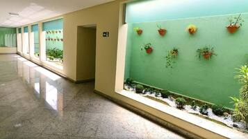 Um corredor com paredes verdes, plantas em vasos e chão de azulejos.