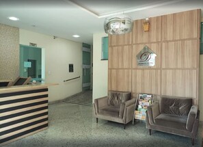 A hotel reception area with a reception desk, two sofas, a chandelier, and a sign for the Domus Hotel. - Domus Cidade Nobre (Ipatinga)