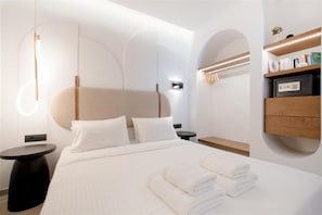 A modern hotel room with a large bed, bedside tables, a built-in shelf with books, and a unique ceiling design. - Vaya Suites (Malevizi)