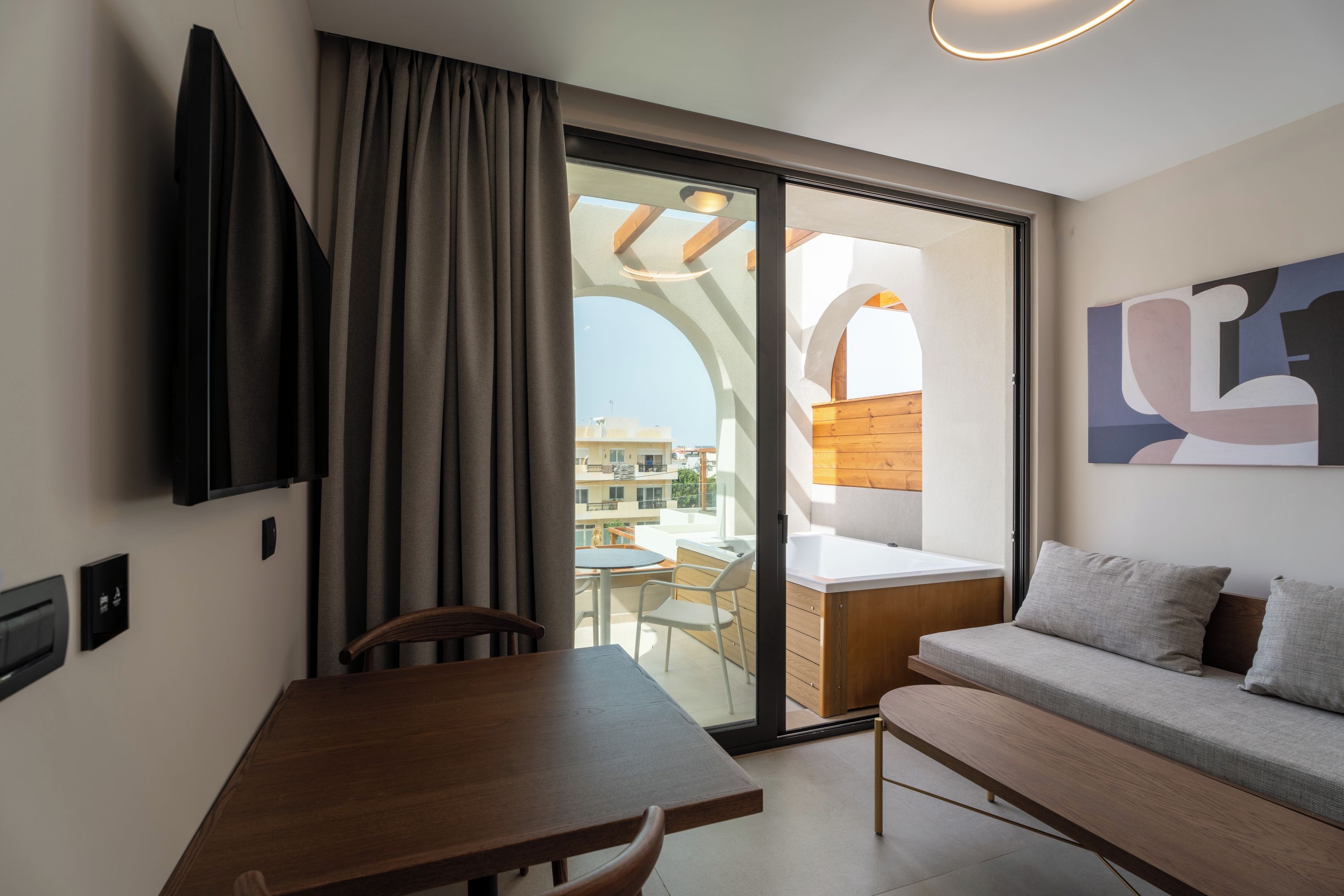 Una habitación moderna con una mesa de comedor, un sofá, un televisor y un ventanal corredera a un área exterior.
