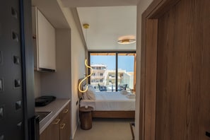 A modern hotel room with a large bed, a small bedside table, a built-in wardrobe, and a view of the city through large windows. - Vaya Suites (Malevizi)