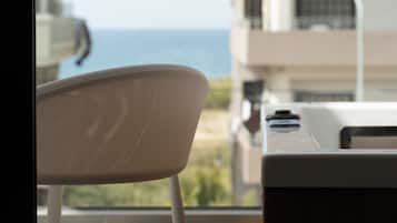 Una silla con respaldo de malla, una ventana con vista al mar y un edificio con balcones.