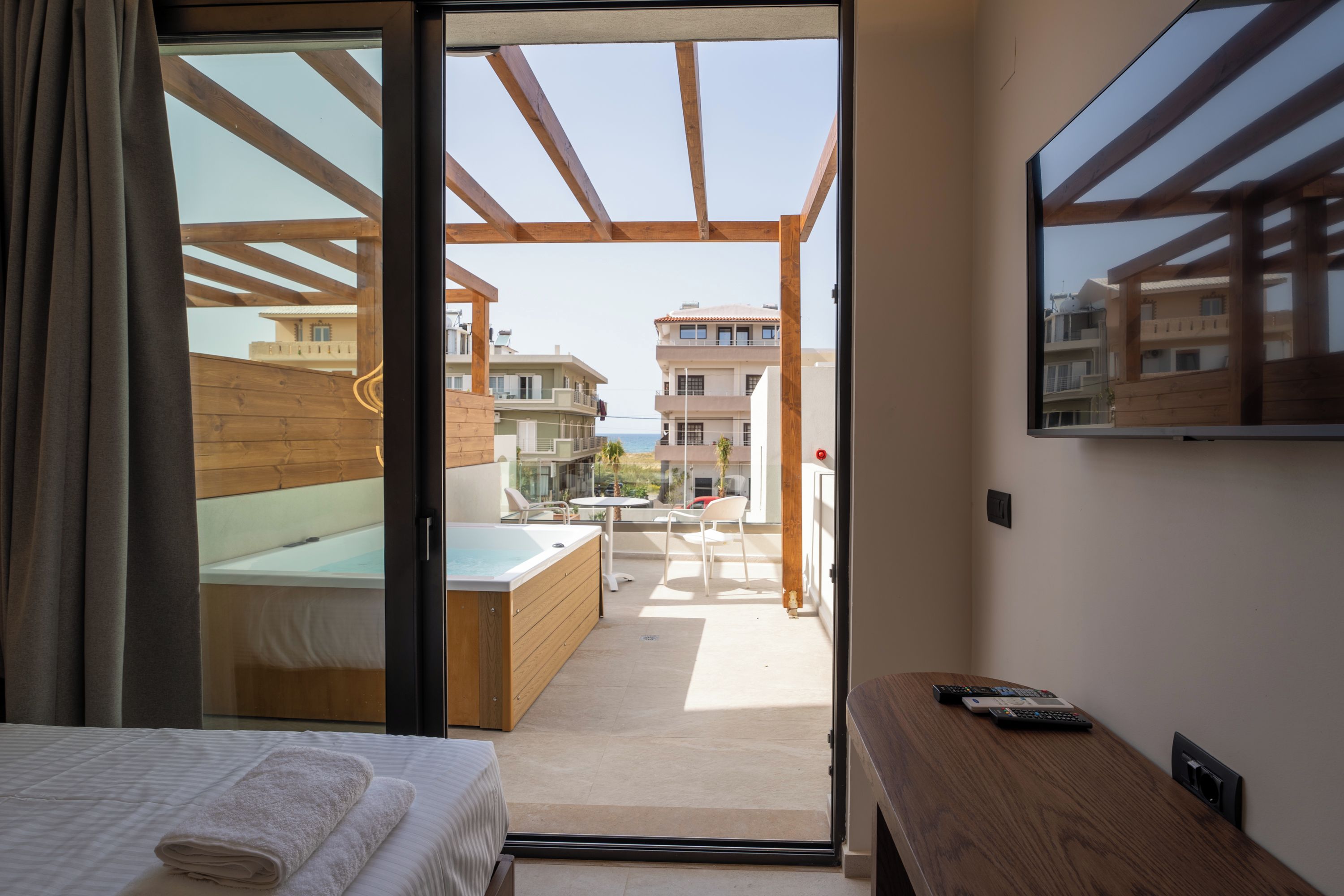 Un dormitorio con cama, un banco de madera, un televisor y vistas al patio exterior.