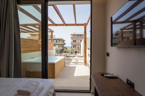 A bedroom with a bed, a wooden bench, a TV, and a view of the outdoor patio area.