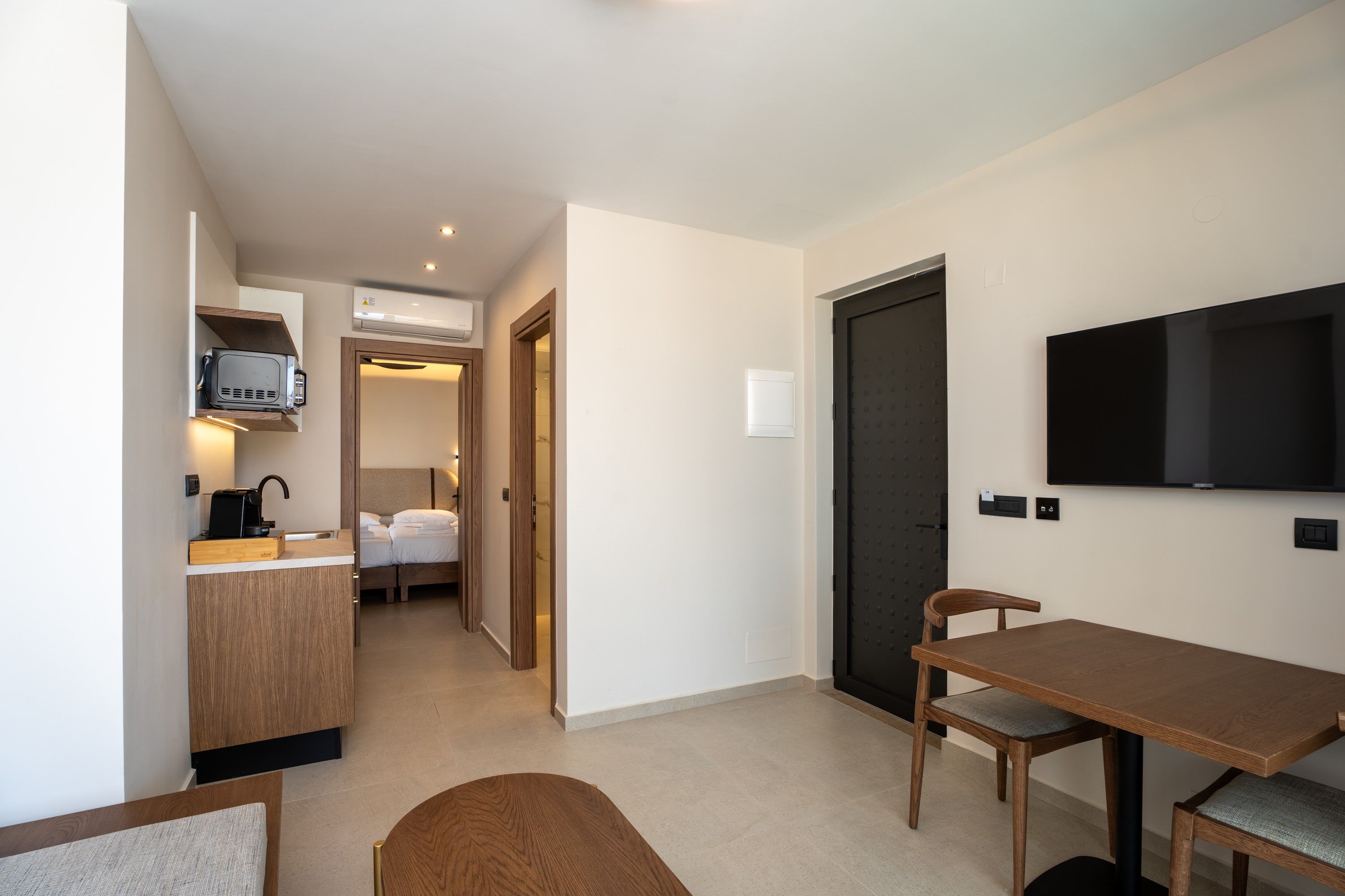 Una habitación de hotel moderna con kitchenette, zona de comedor, televisor y cama.