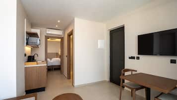 Una habitación de hotel moderna con kitchenette, zona de comedor, televisor y cama.