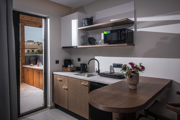A modern kitchen with wooden cabinets, a built-in microwave, and a small dining area with a wooden table and chairs. - Vaya Suites (Malevizi)