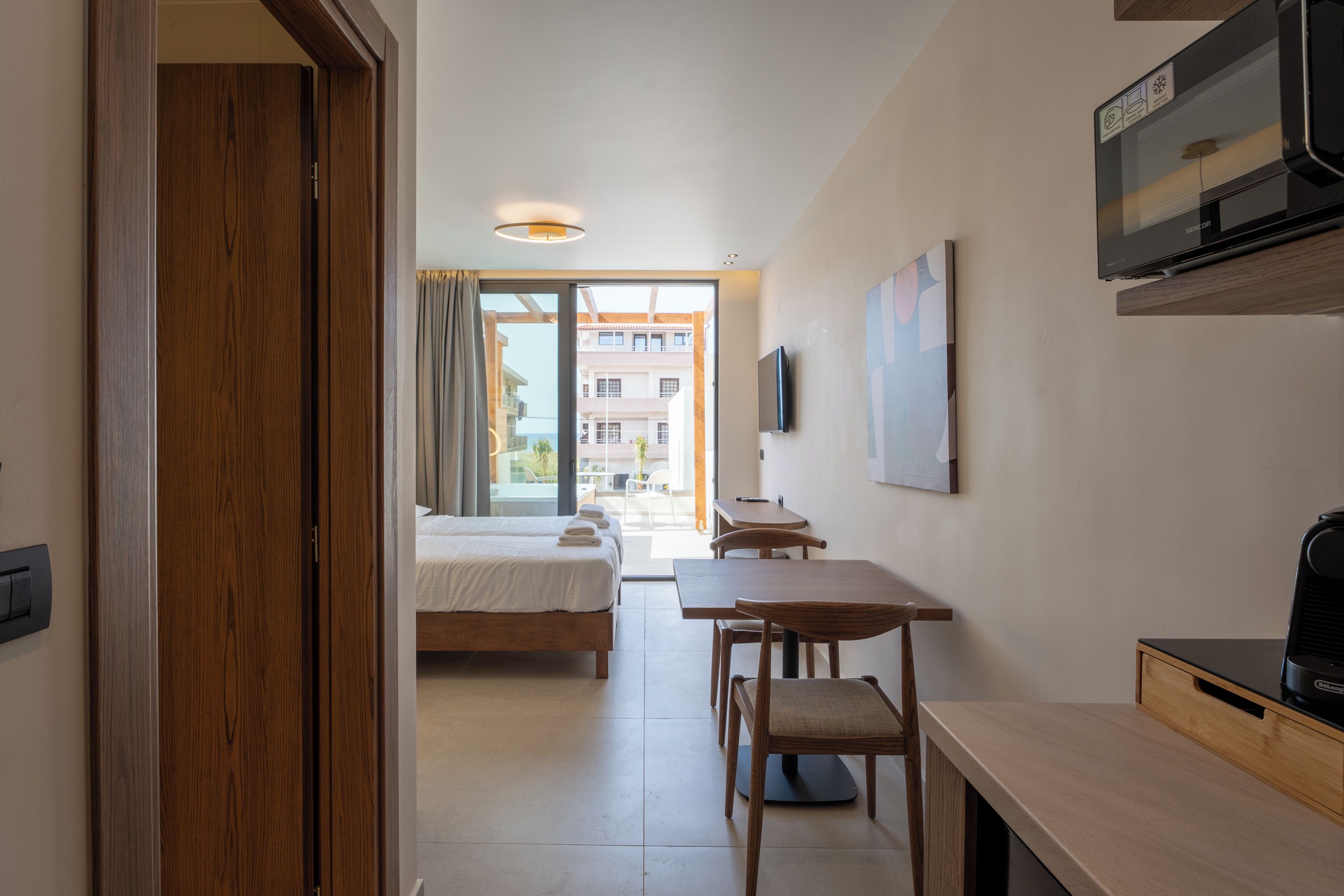 Quarto de hotel com cama, escrivaninha, cadeira, televisão e janela.