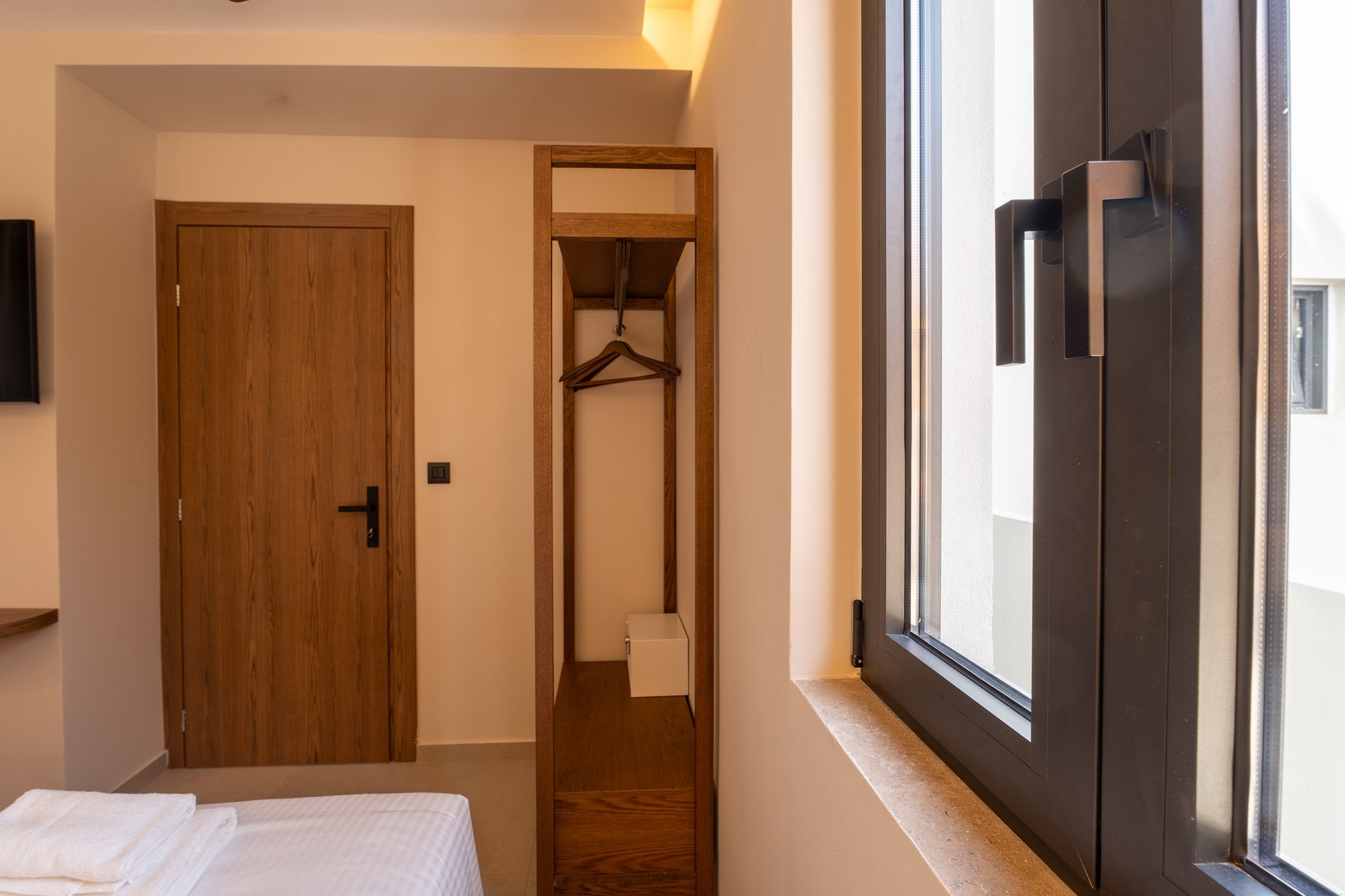 A bedroom with a bed, a wooden door, a closet with a hanging rack, and a window with a view of the outside.