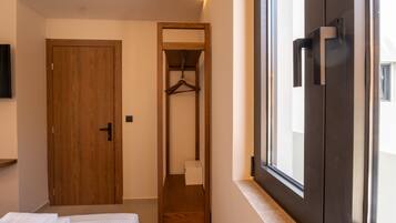 Un dormitorio con cama, puerta de madera, armario con perchero y ventana con vistas al exterior.