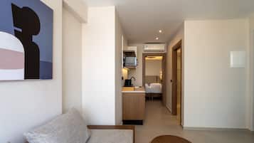 Una habitación de hotel moderna con sofá, una pequeña mesa de madera, una kitchenette y un pasillo que conduce a un dormitorio.