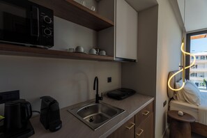 Een moderne kitchenette met een magnetron, koffiezetapparaat en waterkoker, een roestvrijstalen spoelbak en een kleine tafel met een lamp.
