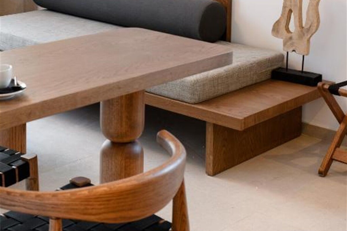 A modern room with a wooden dining table, a bench with cushions, and a wall-mounted abstract art piece.