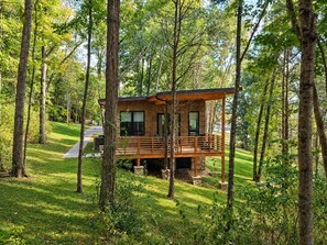 Une cabane dotée d’une terrasse, entourée d’arbres, et un chemin pavé menant à celle-ci.