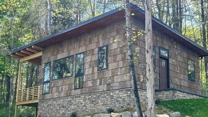 Una cabaña moderna de troncos con cimientos de piedra, ventanas amplias y una terraza de madera.