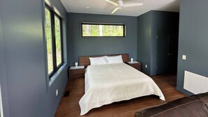 Un dormitorio con cama, mesitas de noche, ventilador de techo, ventana y puerta.