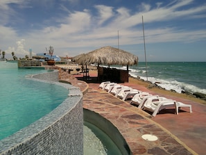 Relax by the serene pool, surrounded by ocean views and a thatched-roof structure.