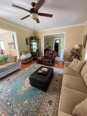 A living room with a ceiling fan, a brown leather chair, a beige sofa, and a patterned rug.
