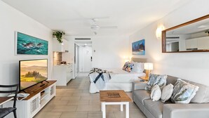 A modern living room with a sofa, a coffee table, a TV, and artwork on the walls. - Belle Escapes  - Drift Beachfront Resort Suite 3402 (Palm Cove)