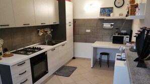 Cocina compacta con gabinetes blancos, estufa a gas, microondas y una pequeña isla con un taburete.