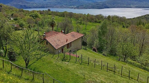 Una casa con techo rojo rodeada de campos verdes exuberantes y montañas al fondo.