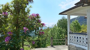 Un espacio al aire libre cubierto con vista a un paisaje montañoso, una cerca blanca y un árbol con flores moradas.