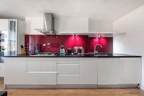 A modern kitchen with white cabinetry, a stainless steel range hood, and a red accent wall.