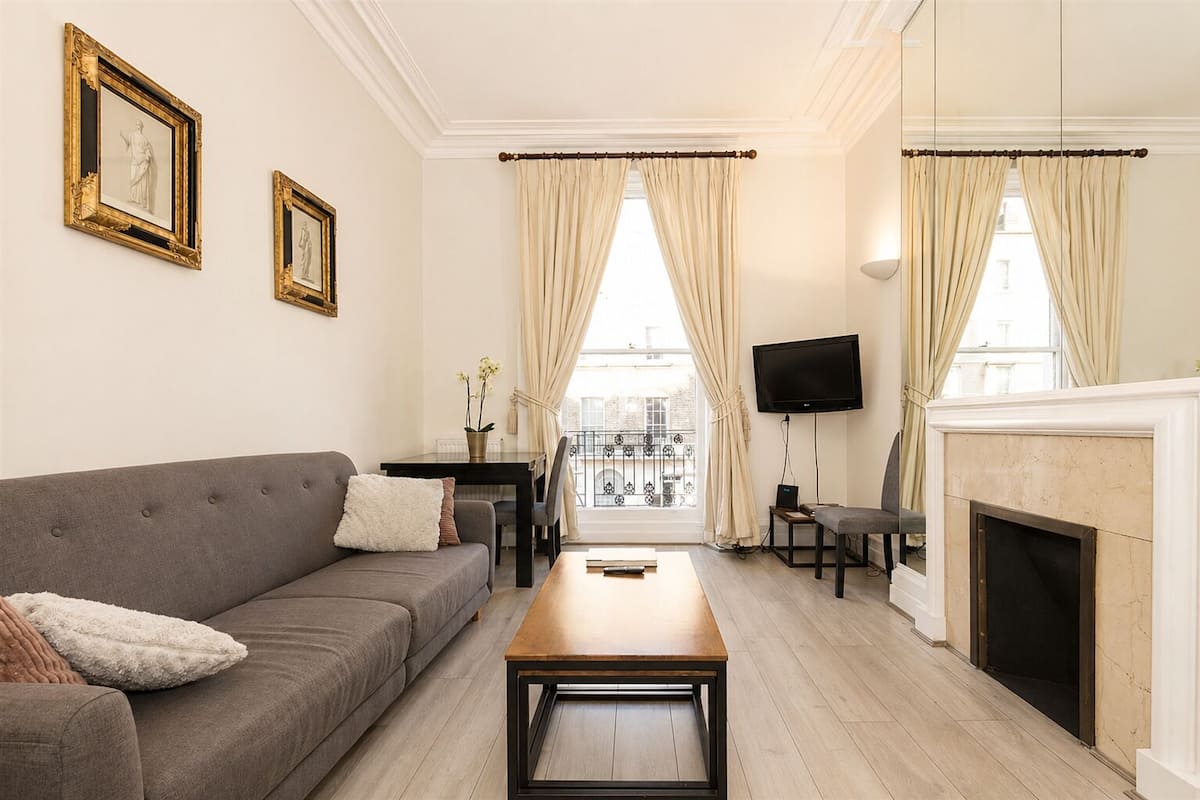 A living room with a sofa, a coffee table, a fireplace, a TV, and a balcony with curtains.