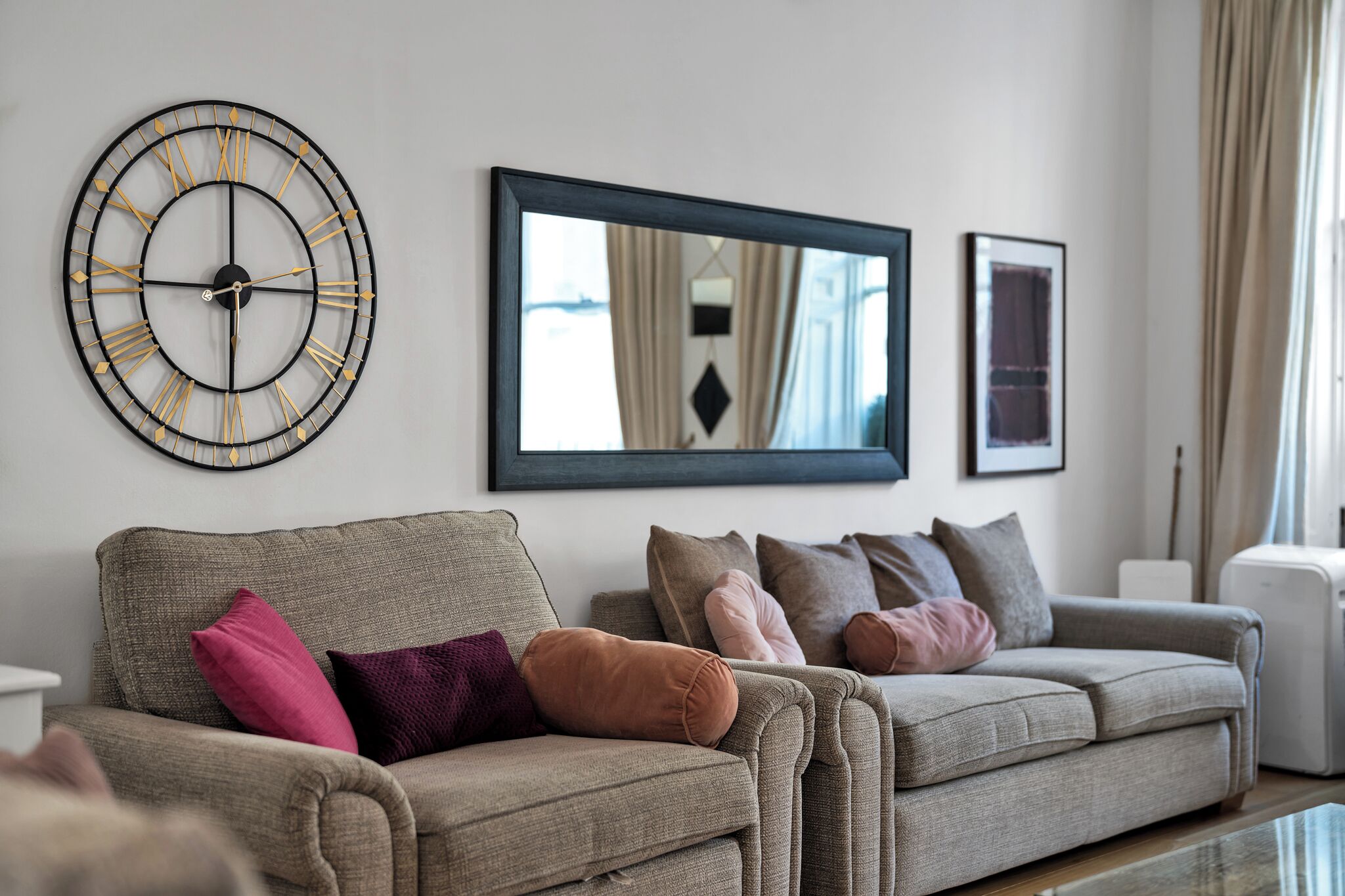 A living room with a large wall clock, a mirror, and two sofas with cushions.