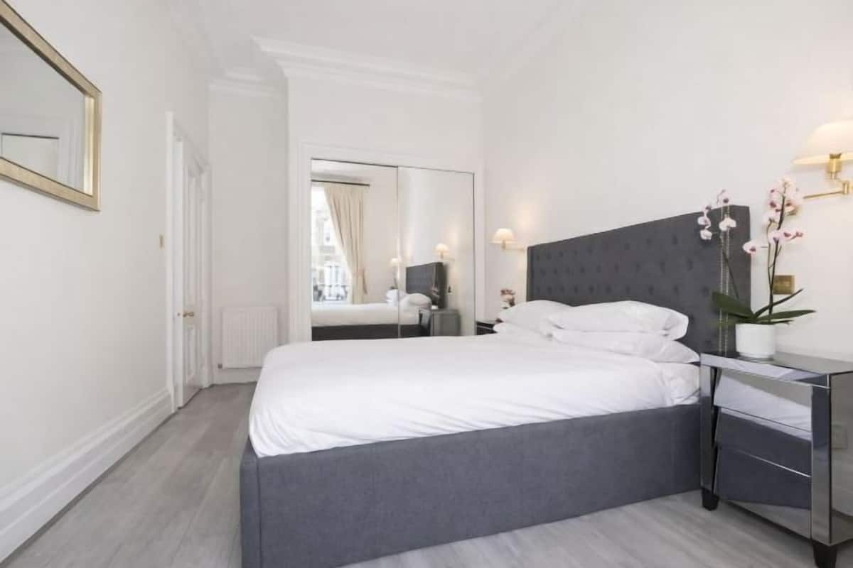 A modern bedroom with a large bed, a nightstand, a mirror, and a potted plant.