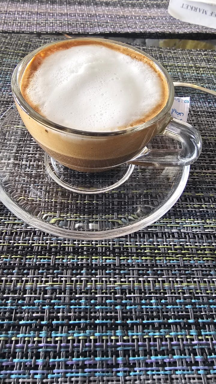 Een transparante koffiemok met schotel op een geweven tafel.