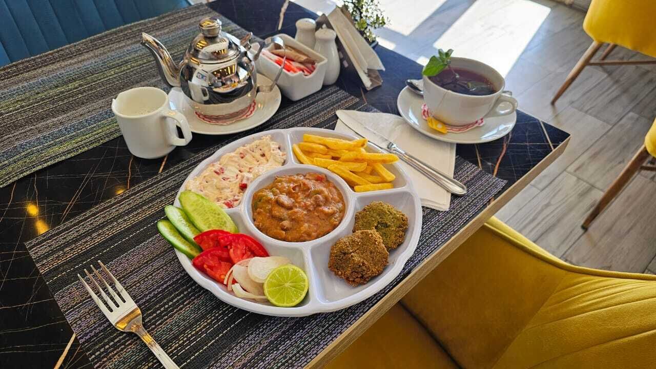A breakfast tray with various foods, a teapot, and cups on a table.