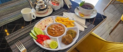 A breakfast tray with various foods, a teapot, and cups on a table.