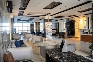 Um hall de hotel moderno com áreas de estar, balcão de recepção e vista para a cidade.