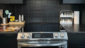 A modern kitchen with a stainless steel stove, black tiled backsplash, and a microwave above. - Entire chalet with Spa near Lake & Beach (Entrelacs)