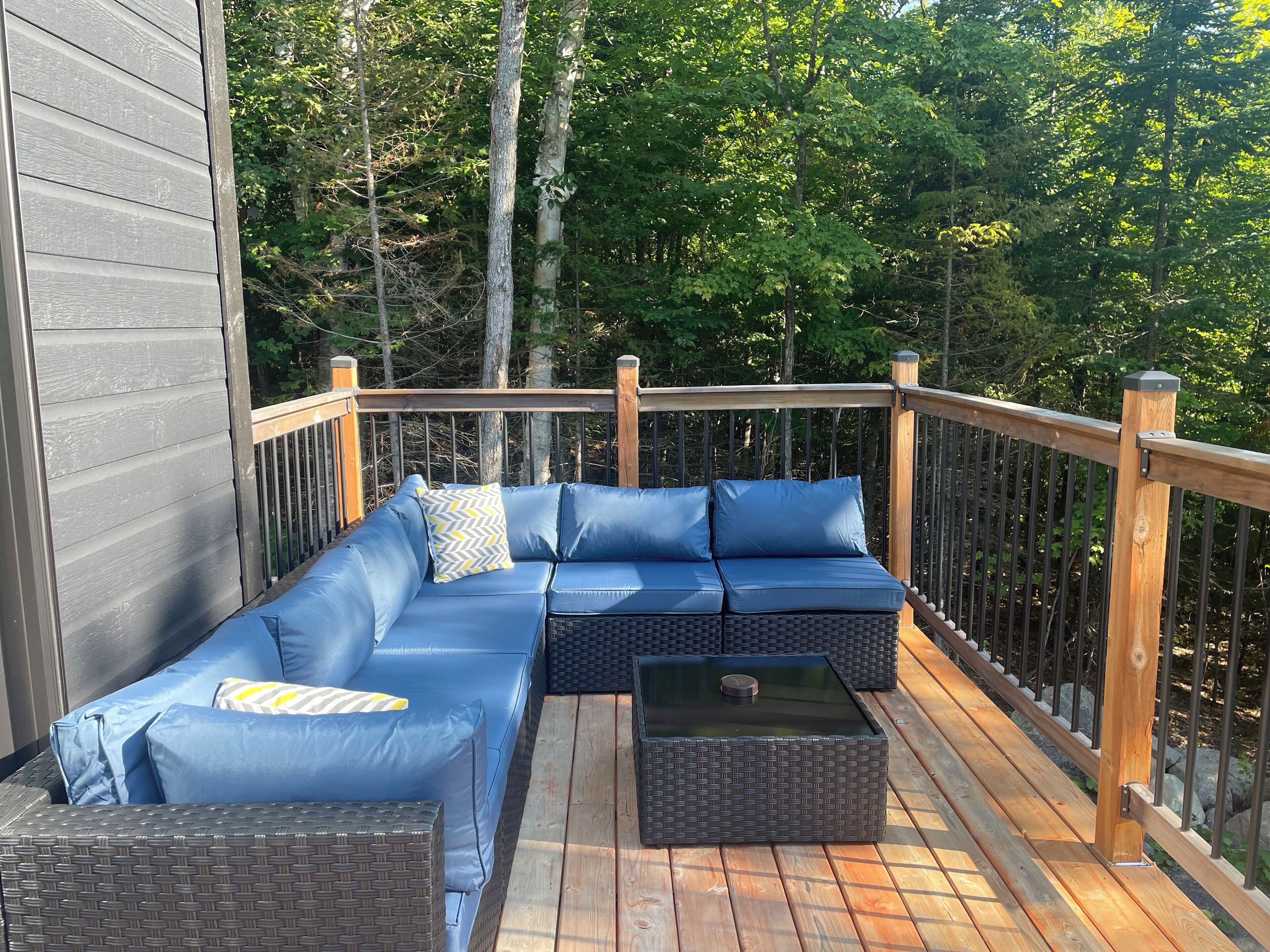 A wooden deck with a blue sectional sofa and a wicker table.