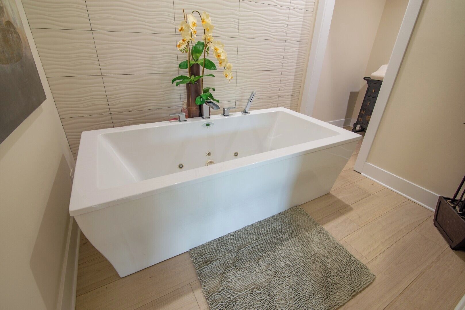 Un baño moderno con una bañera blanca, piso de madera y pared texturizada.