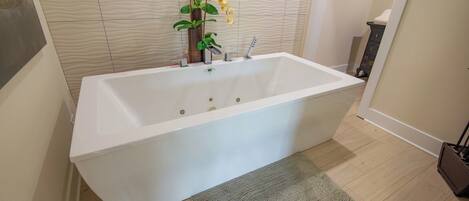 Un baño moderno con una bañera blanca, piso de madera y pared texturizada.