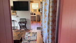 A hallway leading to a dining area with a wooden table and chairs, a television mounted on the wall, and a kitchen area with a window and an air conditioning unit. - Artful Asheville Oasis ~ Private Hot Tub, Fire Pit, Peaceful Wooded Stay (Swannanoa)