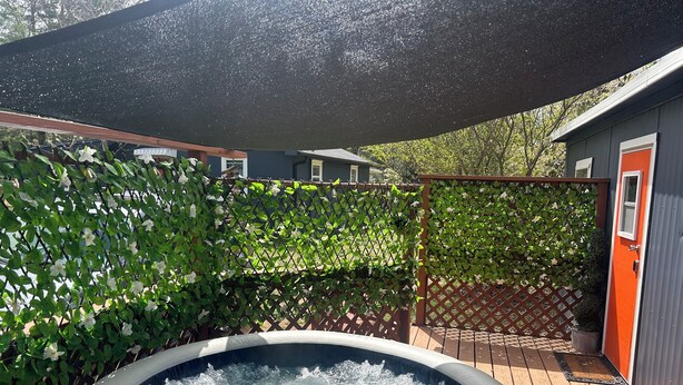 A hot tub surrounded by a wooden deck, a metal fence, and a house with a red door. - Artful Asheville Oasis ~ Private Hot Tub, Fire Pit, Peaceful Wooded Stay (Swannanoa)