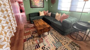 A living room with a green sofa, patterned rug, and a wooden coffee table. - Artful Asheville Oasis ~ Private Hot Tub, Fire Pit, Peaceful Wooded Stay (Swannanoa)