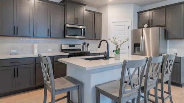 A modern kitchen with grey cabinets, stainless steel appliances, and a central island with bar stools. - 4BR/3.5BH Private Pool: 5M Airport, F1 & 2-Story (Austin)