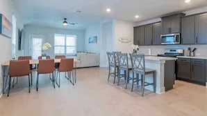 A spacious kitchen with grey cabinets, a central island, and a dining area with chairs and a table. - 4BR/3.5BH Private Pool: 5M Airport, F1 & 2-Story (Austin)