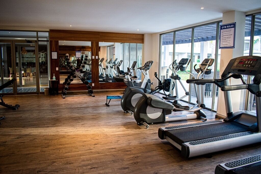 Un gimnasio con cintas de correr y bicicletas estáticas, suelo de madera y amplios ventanales con vistas al exterior.