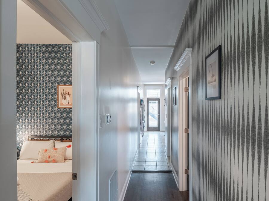 Un couloir avec un mur orné de motifs, une porte donnant sur une chambre et un escalier au fond.