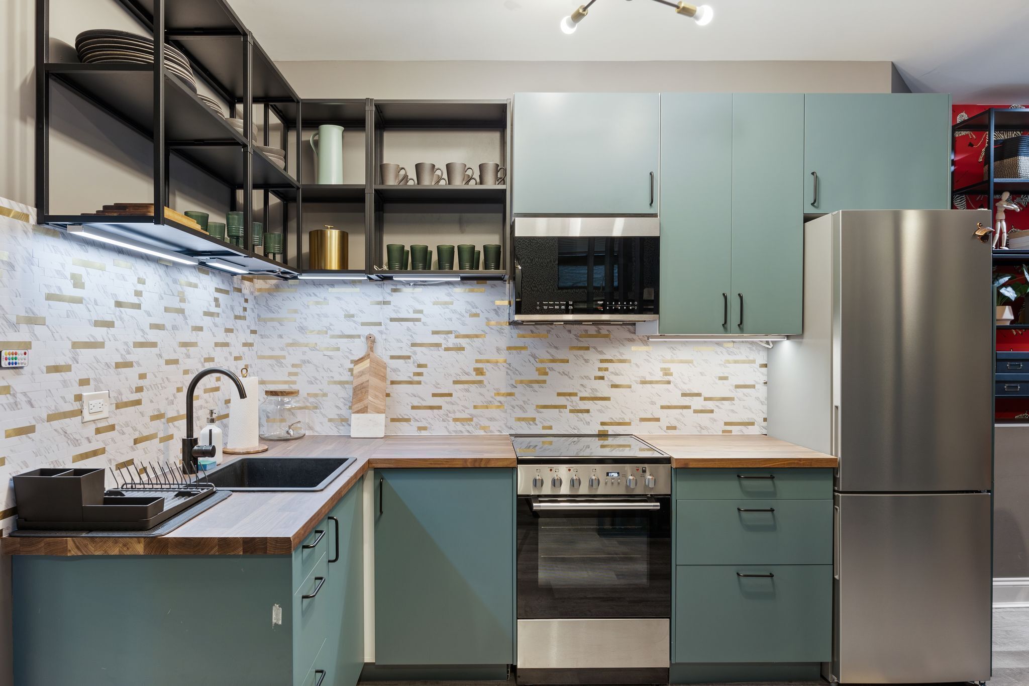 A modern kitchen with teal cabinets, a stainless steel refrigerator, a built-in oven, and a microwave.